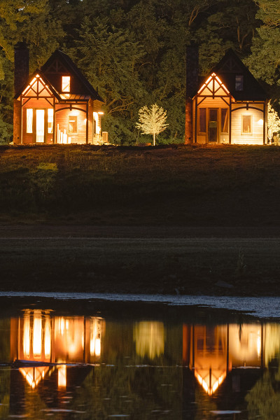 Four cabins lit up at night, reflected in water