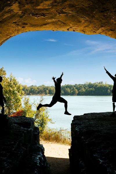 A person jumps across a rock with friends, blue sky and water in the background