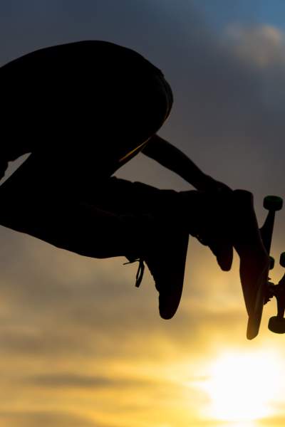 A skateboarder jumps high in the air against the setting sun at a Chicago skate park.