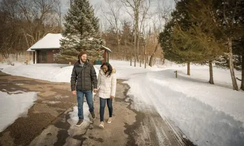 A couple walk along a path surrounded by snow