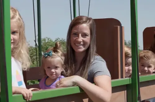 An adult and a young child smiling while enjoying a train ride at a pumpkin patch. 