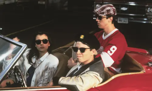 Still image from the movie Ferris Bueller's Day Off, with the three leads sitting in an open-top red Ferrari