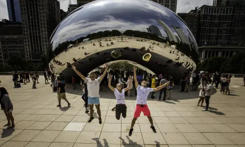 Three people jumping up in the air in front of The Bean landmark in Chicago