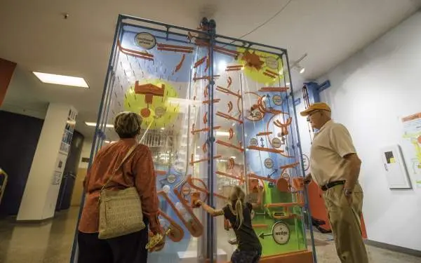 A child playing with an interactive museum exhibit, as grandparents watch on