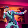 A blues singer wearing a classy metallic suit on stage belting out a song