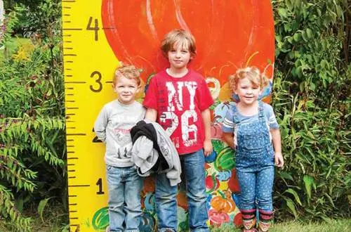 3 kids standing next to a measuring post