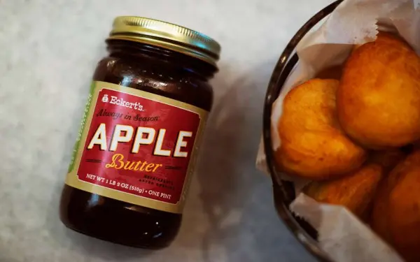 A jar of apple butter next to a fruit bowl of apples