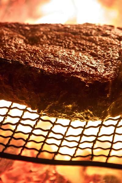 A large steak being cooked on a wire rack over open flame