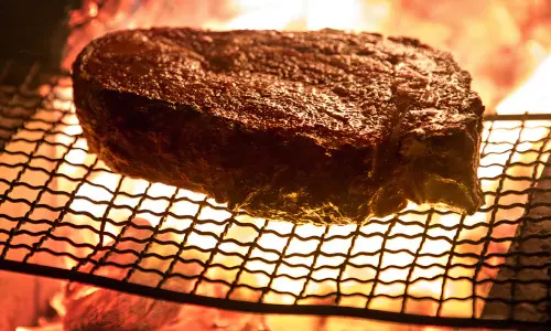 A large steak being cooked on a wire rack over open flame