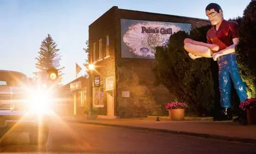 Sunsetting behind a car with a giant statue of a man holding a hotdog