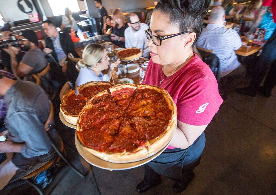 A Giordano's server carrying two deep dish pizzas through a busy restaurant