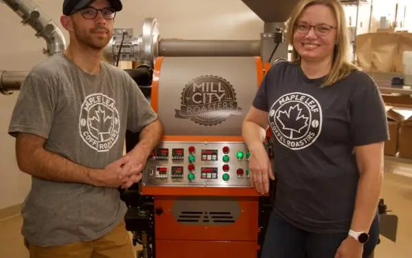 Woman and a man standing by coffee roasting equipment