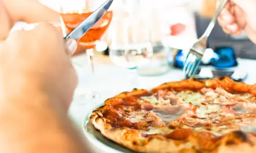 Person eating pizza with a knife and fork