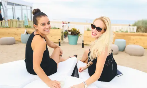 Two women enjoying a drink on a beach lounger
