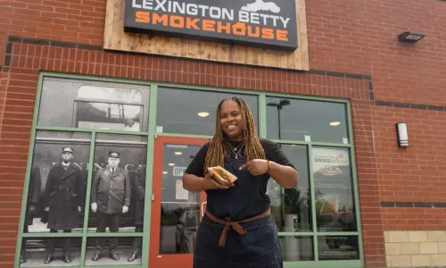 A woman holding a hotdog in front of the Lexington Betty Smokehouse.