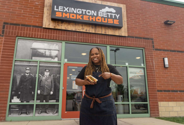 A woman holding a hotdog in front of the Lexington Betty Smokehouse.