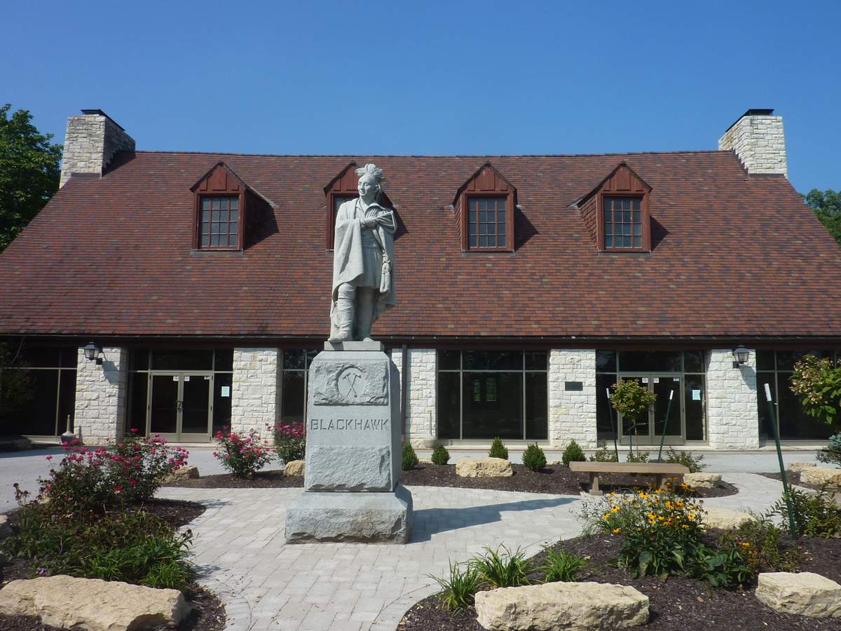 A statue of Blackhawk in front of a low-profile two-storey building