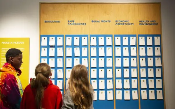 Kids looking up at the make a pledge board covered in tiles at the Holocaust Museum 