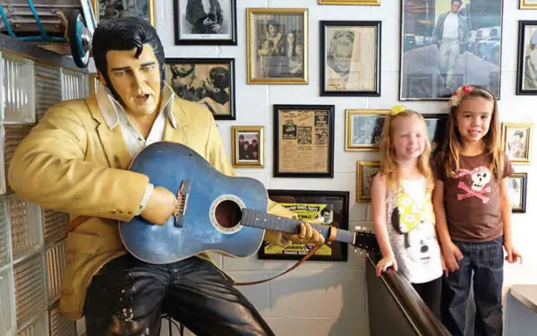Two young kids getting a photo next to a statue of Elvis Presley holding a guitar 