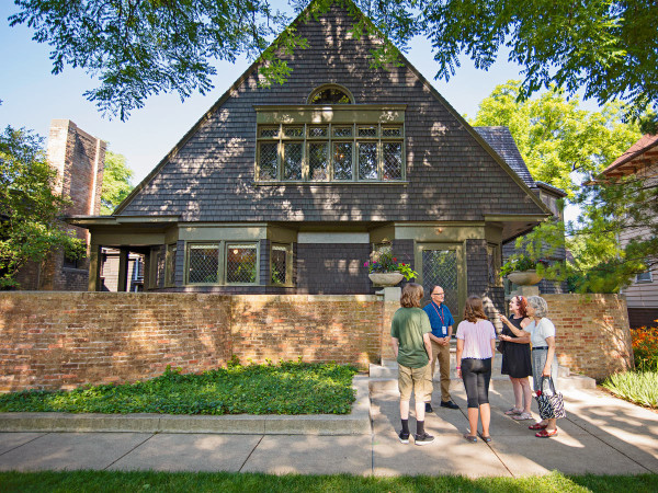 A guide speaks to a tour group on the sidewalk in front of Frank Lloyd Wright's house and studio in Oak Park