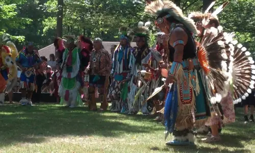 A group of men in Native American attire on a grass clearing amid trees