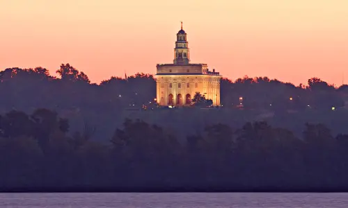 A temple with lights on behind trees and a river