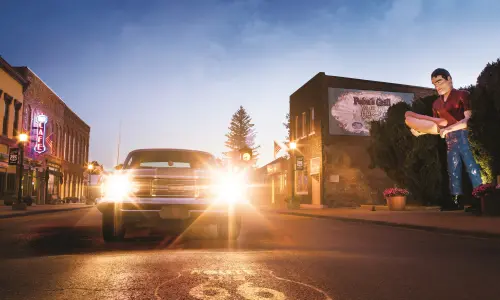 A classic car with its headlights on, alongside the giant Paul Bunyon statue in Atlanta
