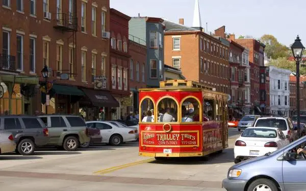 A red trolley bus drives down the main street of Galena, surrounded by parked cars and brick buildings