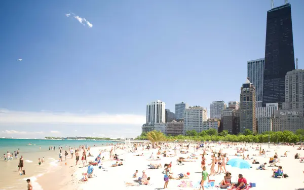 Crowds of people on Oak Street Beach, Chicago, on a sunny day. Chicago skyscrapers are in the background.