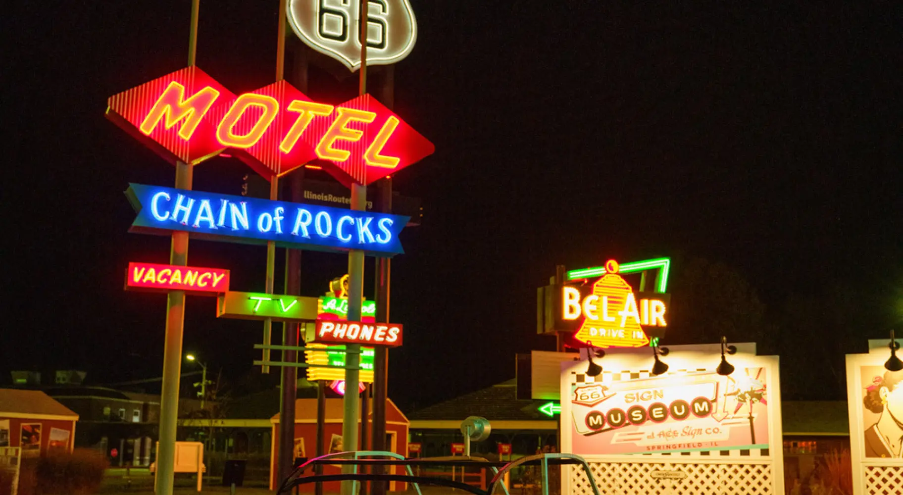 Vintage neon Route 66 motel signs and a classic pedal car illuminated at night.