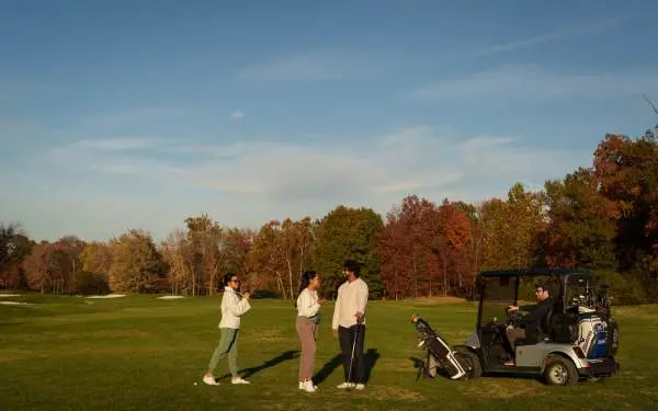 Friends talking on a golf course, next to a golf cart