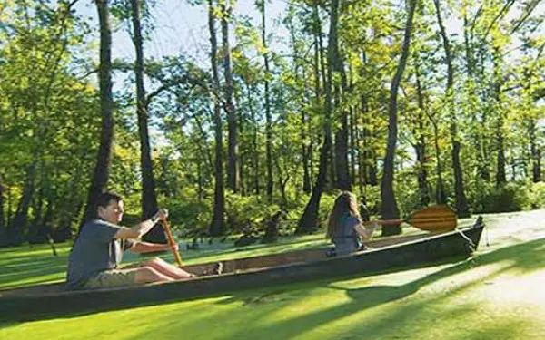 A side on image of a father and daughter canoeing down a swamp river