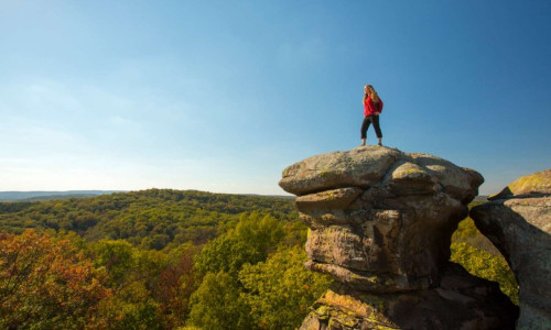 Hiker on top of a large rock over looking the forest.