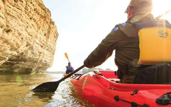 A man in a red kayak paddling around a rock formation