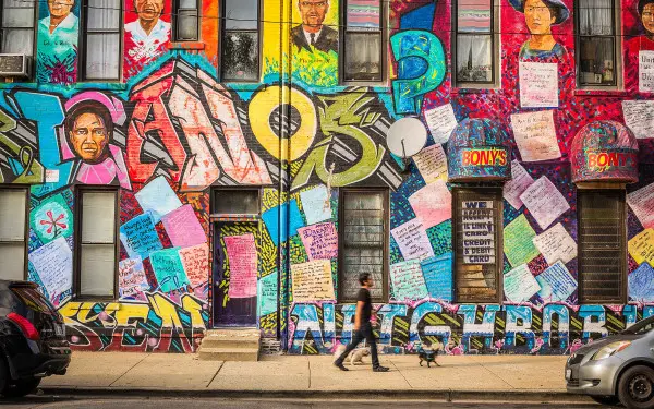 A person with a dog walking in front of a Mexican Heritage Mural