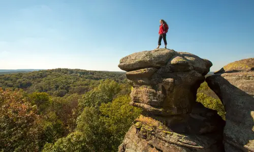 Woman standing on a large rock overlooking the forest below