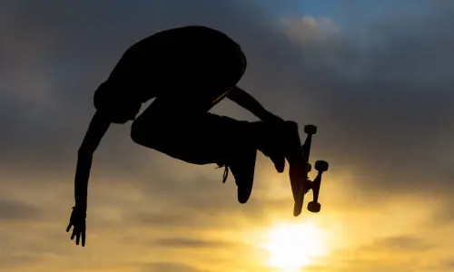 A skateboarder jumps high in the air against the setting sun at a Chicago skate park.