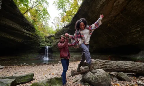 Two people climbing on rocks in front of a rock waterfall
