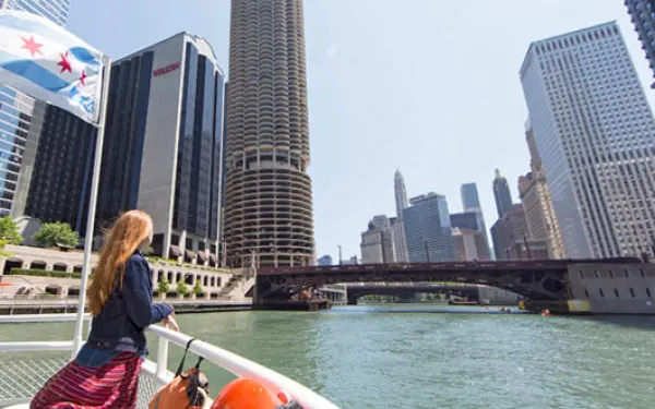 A woman leans on the railing of a river cruise boat on the Chicago River, looking at the city buildings.