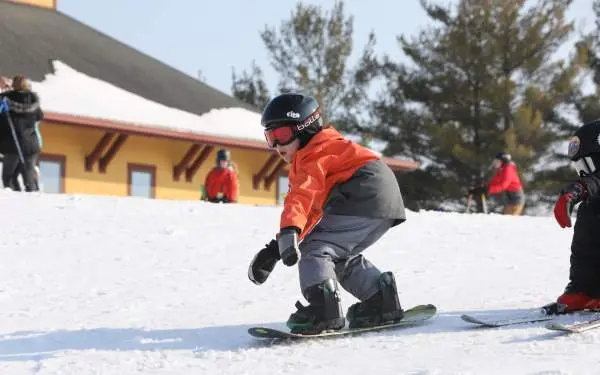 A small child riding a snowboard on snow, wearing a helmet, goggles, and warm ski clothing