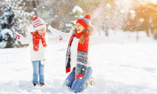 A mother with her child dressed warmly for the weather and throwing snow in the air