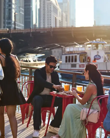 A couple enjoys food and drinks at an outdoor riverside patio. 