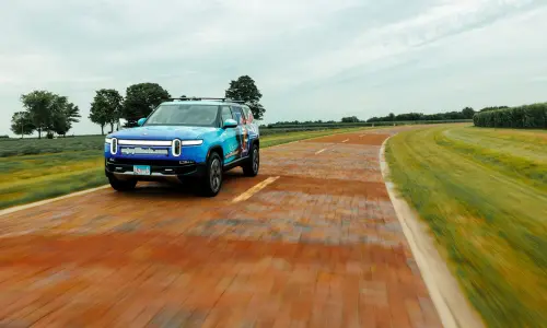 A Rivian drives along a brick road