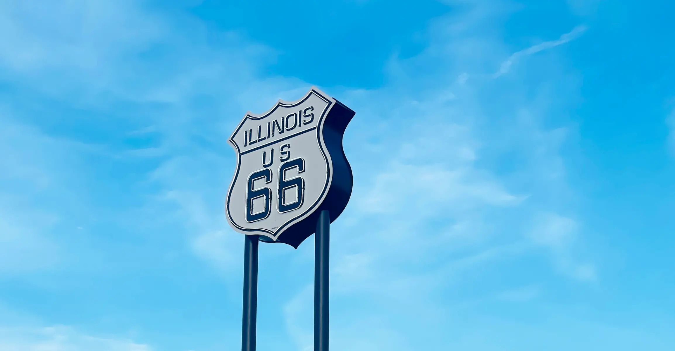 A neon Route 66 sign on two poles against a blue sky