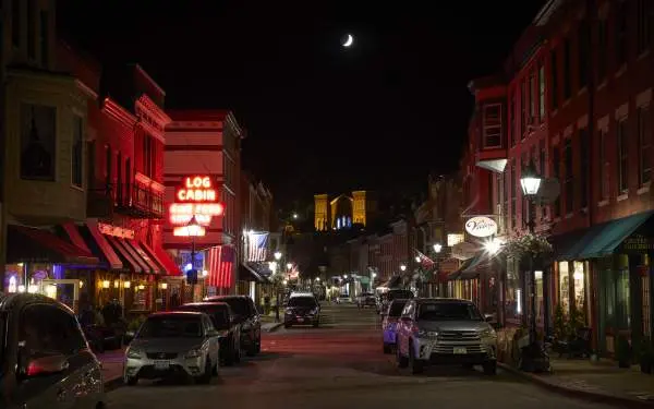 Main street of a small town at night, with cars on either side of the road and a bright neon sign that reads "Log Cabin"