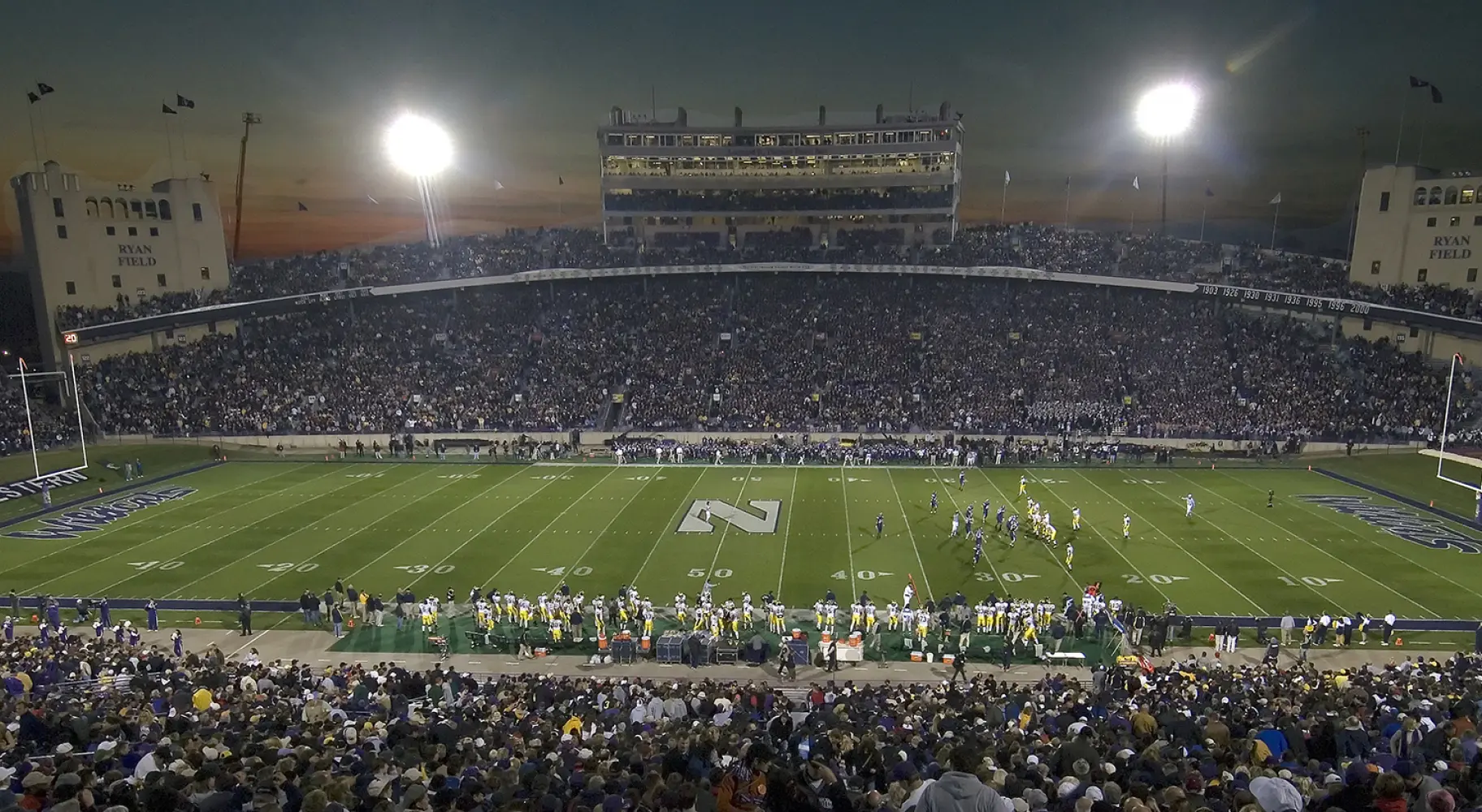 A large college football stadium at night before a game, stands full of spectators