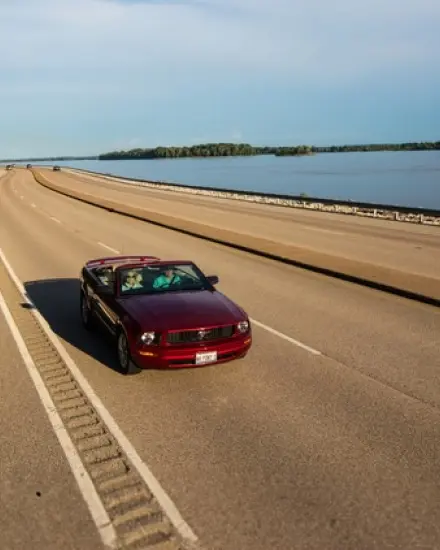 Red convertible driving along a scenic highway beside the Mississippi River.