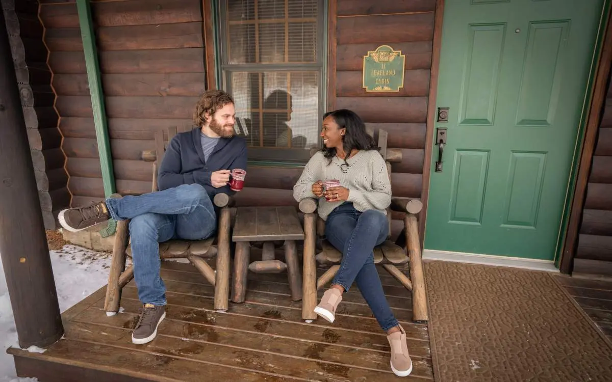 Couple with hot drinks sitting on a deck with snow
