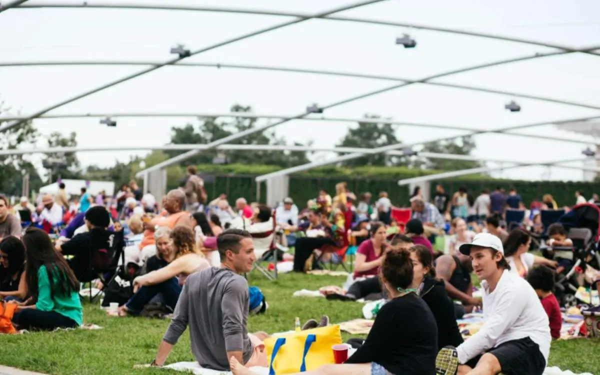 A large audience sitting on the grass outside the Pritzker Pavillion