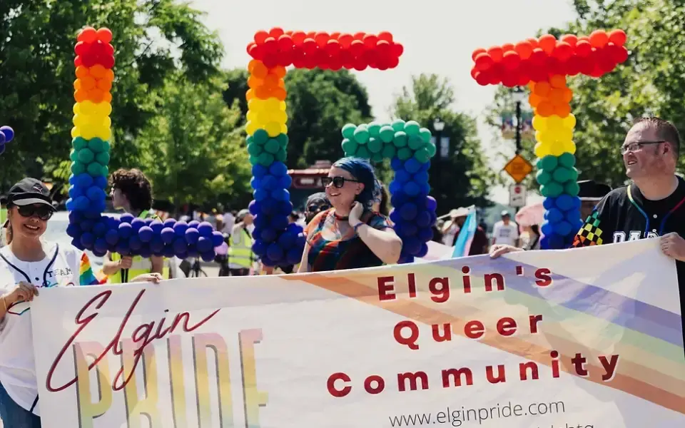 Parade walkers hold a Pride banner and colorful letters